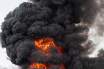 View of flames of red-orange fire and motion clouds of black smoke covered sky. Selective focus, motion blur from strong fire and high temperature from flames.