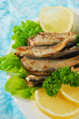 Pan-fried spiced sprats with lemon, salad on a plate