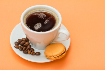 Cup of coffee with coffee beans and delicious macarons cake on peach background.