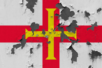 Close up grungy, damaged and weathered Guernsey flag on wall peeling off paint to see inside surface.