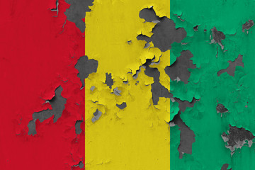 Close up grungy, damaged and weathered Guinea flag on wall peeling off paint to see inside surface.