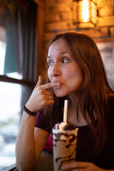 redhead girl drinking a chocolate milkshake at a bar, enjoying it by sucking a finger
