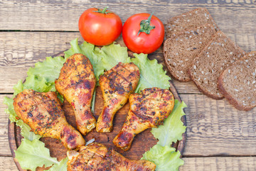 Grilled chicken legs and lettuce leaves on wooden chopping board.