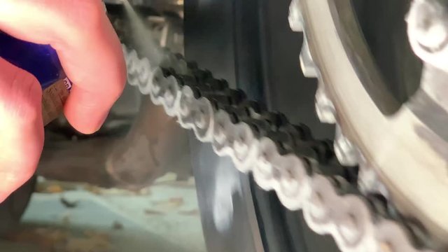 Slowmotion closeup of spraying motorbike chain with oil lubricant. Oiling a motorcycle chain in a workshop. Woman is lubricating moto chain with lube.