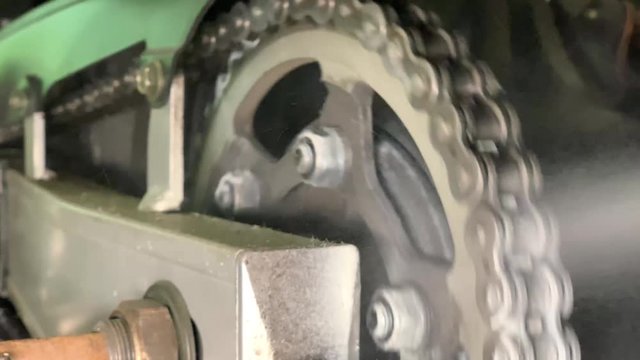 Woman is lubricating moto chain with lube. Closeup of spraying motorbike chain with oil lubricant. Oiling a motorcycle chain in a workshop.