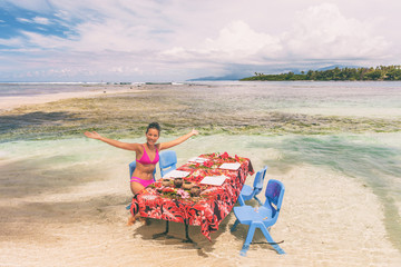 Beach picnic motu tour in Bora Bora, Tahiti, French Polynesia. Happy tourist woman eating at table in ocean water feet in sand for summer lunch. Travel lifestyle. - obrazy, fototapety, plakaty