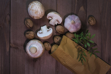 Fresh vegetables and nuts are on the table. Nuts in a paper bag, near champignons and onions with garlic, green broccoli with a sprig of seasoning