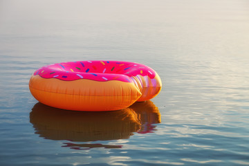 Big inflatable donut on water in sunrise time. Hipster sprinkled donut float in lake