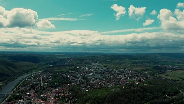 aerial view of zbraslav under clouds next to river and mountains in the background