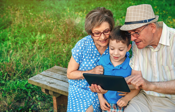 Grandparents using the tablet with their grandson sitting on a bench outdoors