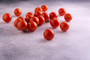 Bunch of cherry tomatoes on white textured stone concrete table, side view with copy space. Ingredients for cooking.