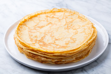 Crepes, thin pancakes with honey on a white plate. Marble background. Close up.