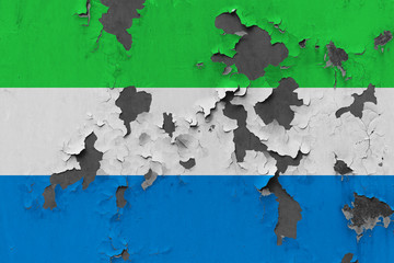 Close up grungy, damaged and weathered Sierra Leone flag on wall peeling off paint to see inside surface.