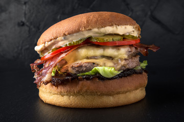 Juicy fresh delicious hamburger with beef steak, fried bacon, cheese dorblyu, caramelized onions, lettuce, sauce on a fresh bun on the background of coals. The burger menu.