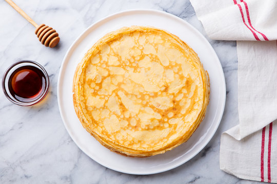 Crepes, thin pancakes with honey on a white plate. Marble background. Top view.