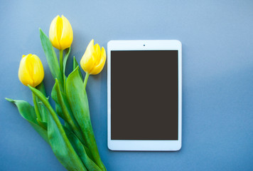 Bouquet of beautiful yellow tulips and tablet on violet background with copyspace. Spring concept.