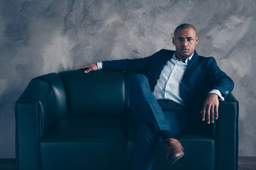 Portrait of his he nice stylish classy chic attractive experienced guy professional top manager ceo boss chief banker sitting on couch at workplace station gray concrete wall