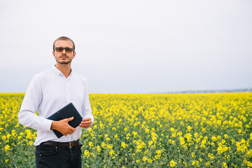 Young agronomist holds tablet in rape field. Agribusiness concept. agricultural engineer standing...