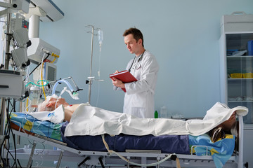 Intensive care caucasian doctor examines intubated critical stance patient writing notes to case report in intensive care department