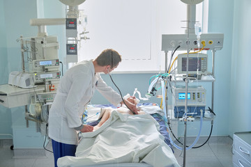 Intensive care caucasian doctor examines intubated critical stance patient in intensive care department