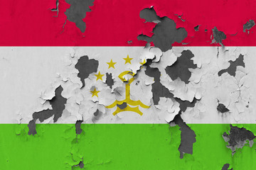 Close up grungy, damaged and weathered Tajikistan flag on wall peeling off paint to see inside surface.