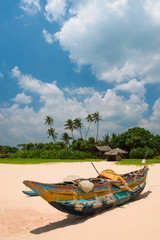 Old fishing boat on the beach with fisherman's shed on background at Sri Lanka.