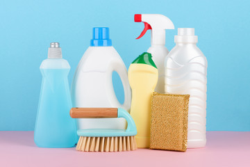 Cleaning supplies assortment. Cleaning brush, plastic bottles with liquids, golden sponge on pink and blue pastel background.