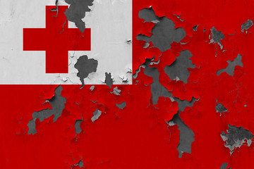 Close up grungy, damaged and weathered Tonga flag on wall peeling off paint to see inside surface.
