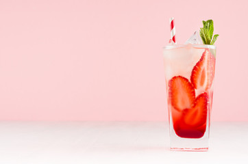 Fresh strawberry cocktail with slices fruits, mint, straw, ice cubes in misted glass on white wood table and pink color wall.