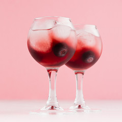 Luxury fresh cold red summer fruit cocktails with ice cubes, blueberry in elegant modern kitchen interior in light soft pastel pink color, square.