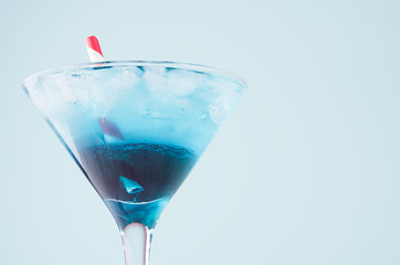 Summer blue cocktail with curacao on misted wineglass with red straw on  green background, closeup, top, edge, details.