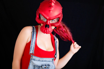 A young woman in denim overalls and red biking helmet on black background.