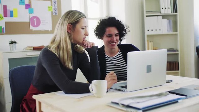 Two young women with laptop working together in a modern office.