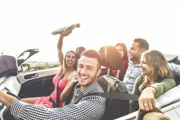 Happy friends having fun in convertible car on summer vacation - Young people laughing and smiling together during travel holidays - Youth lifestyle concept - Main focus on close-up man face - obrazy, fototapety, plakaty