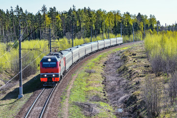 Passenger train approaches to the station at spring morning time.