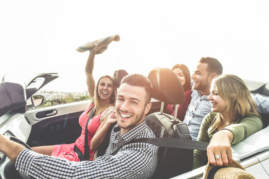 Happy friends having fun in convertible car on summer vacation - Young people laughing and smiling together during travel holidays - Youth lifestyle concept - Main focus on close-up man face - Powered by Adobe