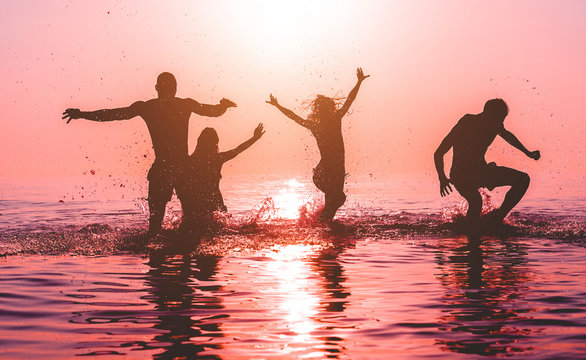 Happy friends jumping inside water on tropical beach at sunset - Group of young people having fun on summer vacation - Youth lifestyle, party and friendship concept - Focus on bodies