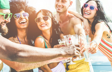 Happy friends cheering with champagne in summer boat party - Young people having fun drinking and laughing together - Youth lifestyle and vacation concept - Focus on left black hand