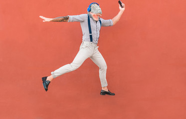 Crazy senior man jumping and dancing rock music wearing t-rex mask - Tattoo trendy guy having fun listening music with headphones - Absurd and funny trend concept - Focus on body