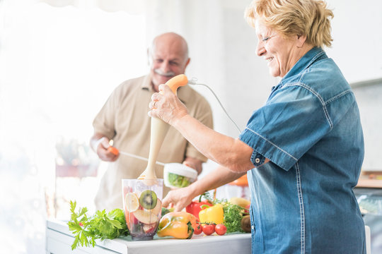 Happy senior couple preparing healthy vegetarian breakfast with fruits and vegetables - Old cheerful people taking care about diet - Health,vegan and organic concept - Focus on woman face