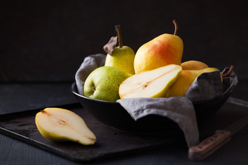 Delicious Williams pears in a black bowl against dark rustic background. Still life, low key