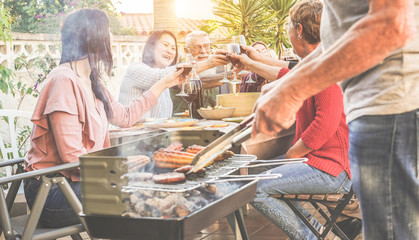Family and friends cheering with wine, grilling meat for at bbq meal outdoor - Different age of...