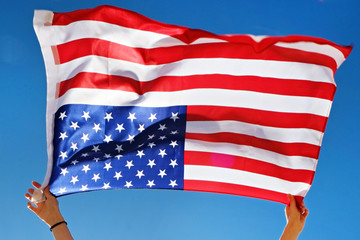 Close up shot of young woman hands holding United State of America flag waving on the wind, clear blue sky. Patriotic background for 4th of july USA Independence day with copy space for text.