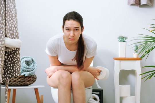 Young woman suffering from constipation on toilet bowl at home