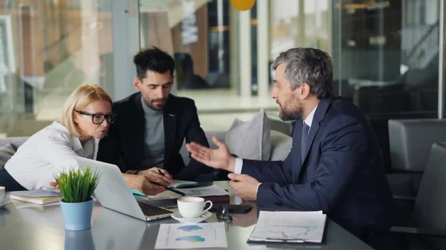 Mad CEO angry bearded man is arguing with employees in cafe during coffee break tearing and throwing papers. Conflict, business and negotiations concept.