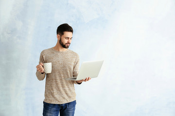 Male programmer with laptop and cup of coffee on color background