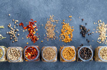 Assortments of spices in jars on grey stone background. Top view. Copy space.