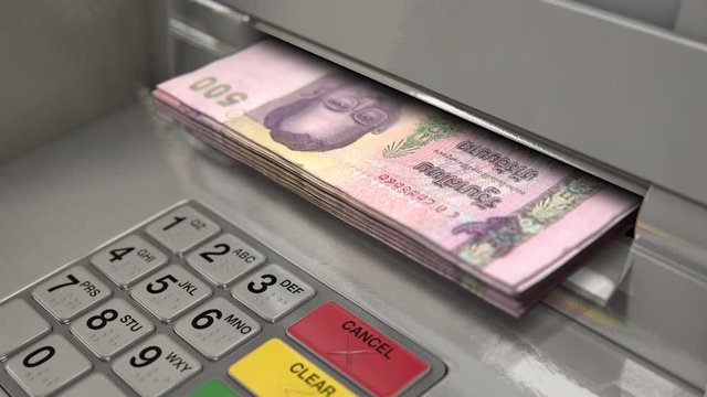 A closeup view of an atm facade with an illuminated sceen and keypad and a wad of thai bhat banknotes being ejected from the cash slot 