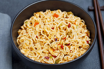Noodles with vegetables in a bowl on grey stone background. Close up.
