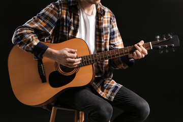Naklejka na ściany i meble Handsome young man playing guitar on dark background